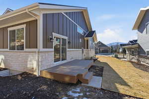 View of side of property featuring board and batten siding, stone siding, a deck with mountain view, and a lawn