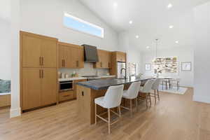 Kitchen featuring an island with sink, a breakfast bar, decorative light fixtures, lofted ceiling, and light wood-style floors