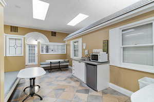 Kitchen with white cabinetry, white microwave, stainless steel fridge, crown molding, and light countertops