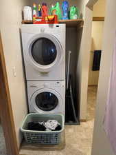 Laundry area featuring stone finish flooring, stacked washer and clothes dryer, and a textured wall
