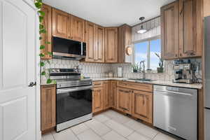 Kitchen with stainless steel appliances, light stone granite countertops, wood finish cabinets, hanging light fixtures, and backsplash
