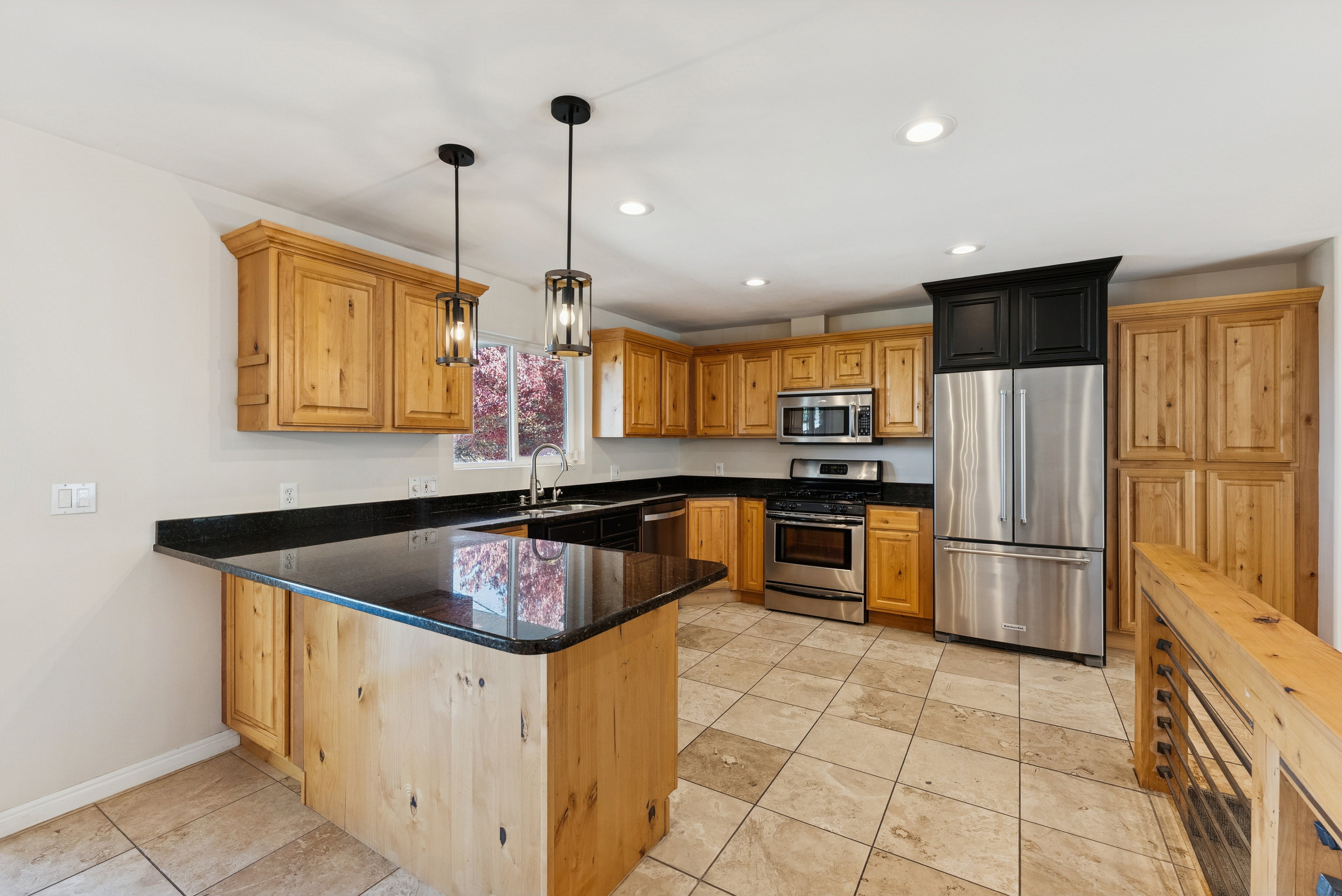 Kitchen featuring stainless steel appliances, dark stone counters, a peninsula, pendant lighting, and wood finish cabinets