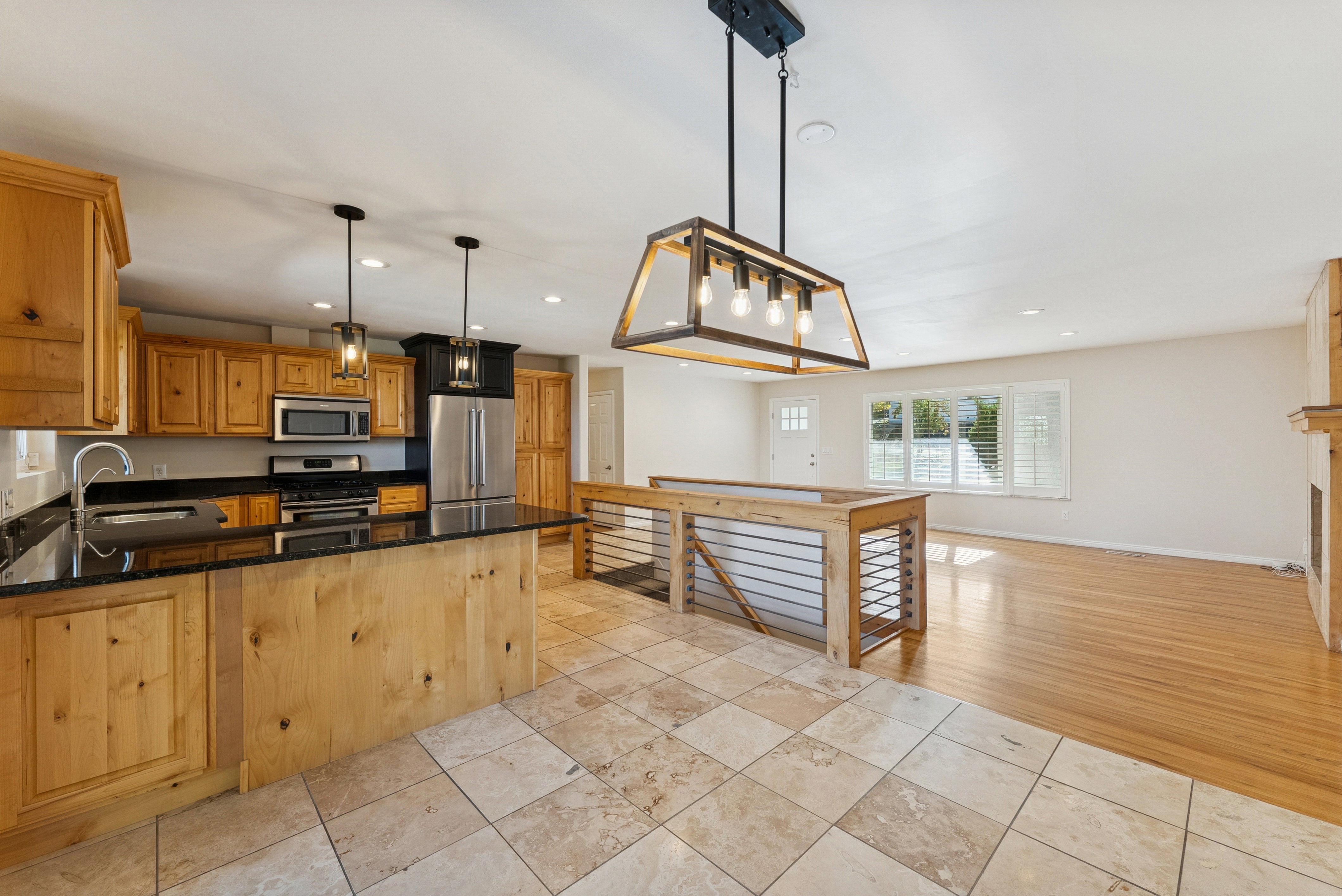 Kitchen with pendant lighting, dark stone counters, stainless steel appliances, wood finish cabinetry, and open floor plan