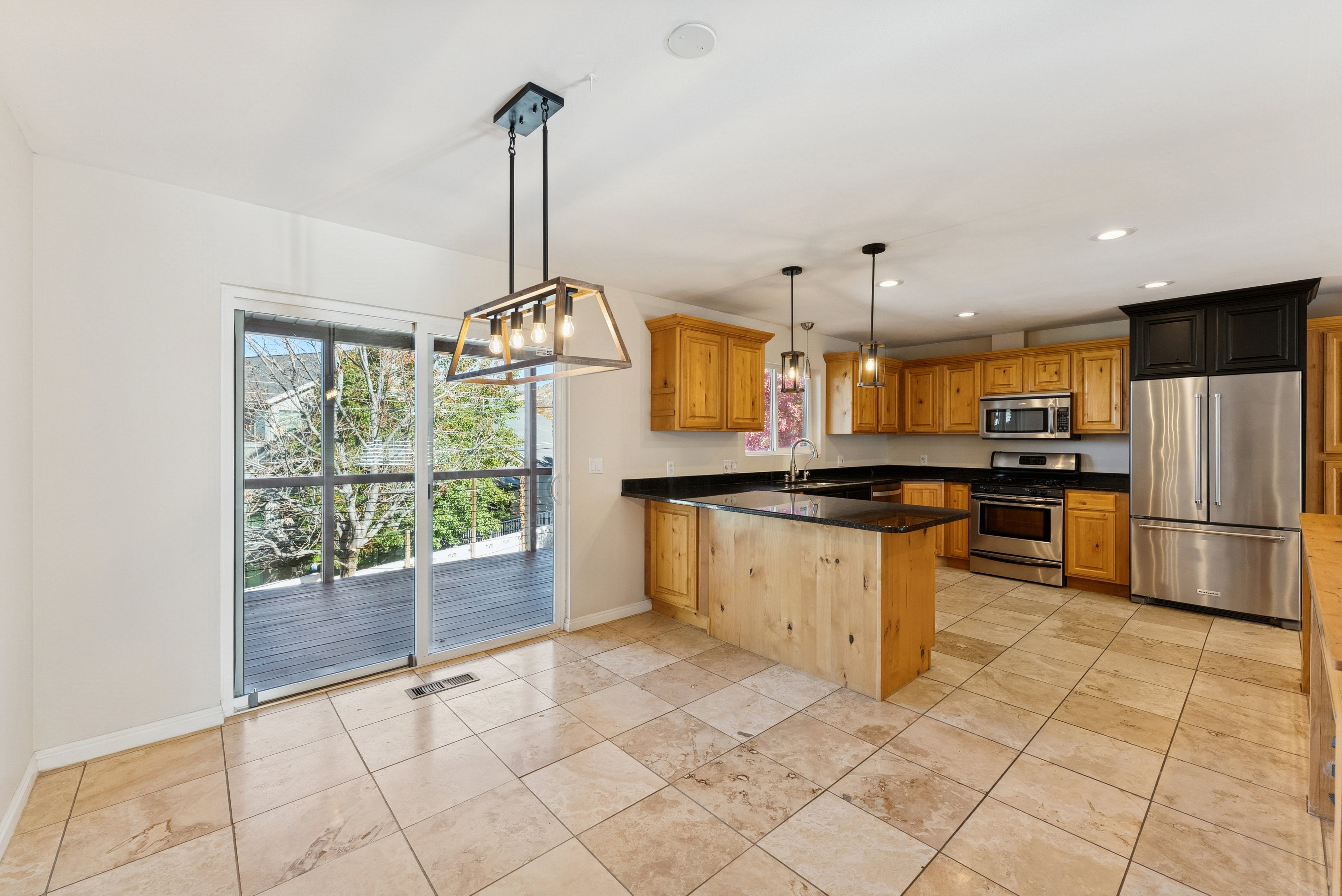 Kitchen featuring stainless steel appliances, wood finish cabinets, a peninsula, dark stone counters, and suspended lighting