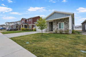 View of front of house with board and batten siding, driveway, stone siding, a front lawn, and a residential view