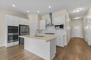 Kitchen with white cabinets, stainless steel appliances, an island with sink, light wood finished floors, and recessed lighting
