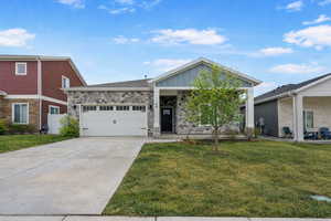 View of front of house featuring board and batten siding, stone siding, a front yard, and an attached garage
