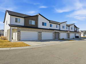 View of front of property featuring stone siding, an attached garage, concrete driveway, and board and batten siding