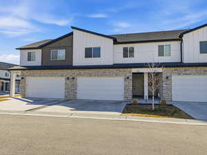 View of front of property featuring stone siding, concrete driveway, and board and batten siding