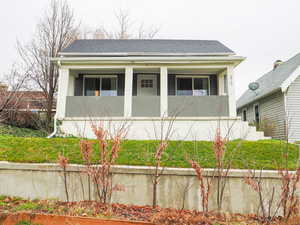 View of front of home with stucco siding, a shingled roof, and a front lawn