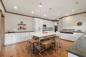 Kitchen with white cabinets, pendant lighting, backsplash, and ornamental molding