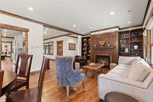 Living room with hardwood / wood-style flooring, a glass covered fireplace, crown molding, recessed lighting, and built in features