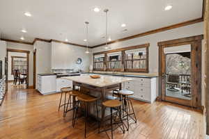 Dual tone kitchen featuring light wood-type flooring, decorative light fixtures, decorative backsplash, crown molding, and dual tone cabinetry
