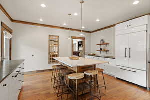Kitchen featuring open shelves, decorative light fixtures, two tone cabinetry, light wood-type flooring, and paneled fridge