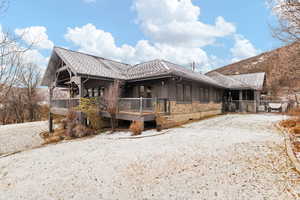 Snow covered property with stone siding and a wooden deck