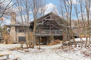 View of front of property with stone siding, a wooden deck, and a chimney