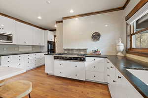 Kitchen with light wood-type flooring, backsplash, stainless steel appliances, white cabinets, and crown molding