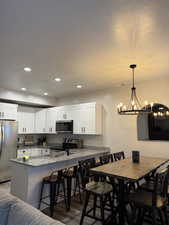 Kitchen with a breakfast bar area, stainless steel appliances, white cabinetry, dark stone countertops, and dark wood-type flooring