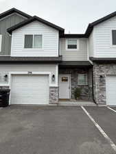 View of front of property with stone siding, a porch, roof with shingles, a garage, and board and batten siding