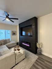 Living room featuring wood finished floors, a ceiling fan, a fireplace, and a textured ceiling