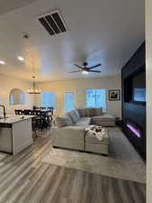 Living room with a textured ceiling, light wood-type flooring, hanging lights, and ceiling fan