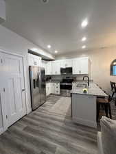 Kitchen featuring a peninsula, light stone countertops, stainless steel appliances, dark wood finished floors, and a kitchen bar