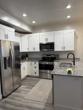 Kitchen with light stone counters, stainless steel appliances, white cabinetry, recessed lighting, and light wood-type flooring