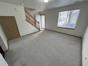 Unfurnished living room featuring stairway and carpet floors