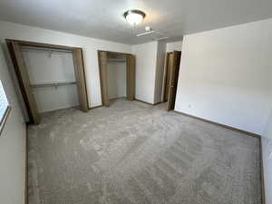 Unfurnished bedroom featuring two closets, carpet flooring, and a textured ceiling