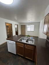 Kitchen featuring a peninsula, white dishwasher, a chandelier, dark countertops, and a textured ceiling