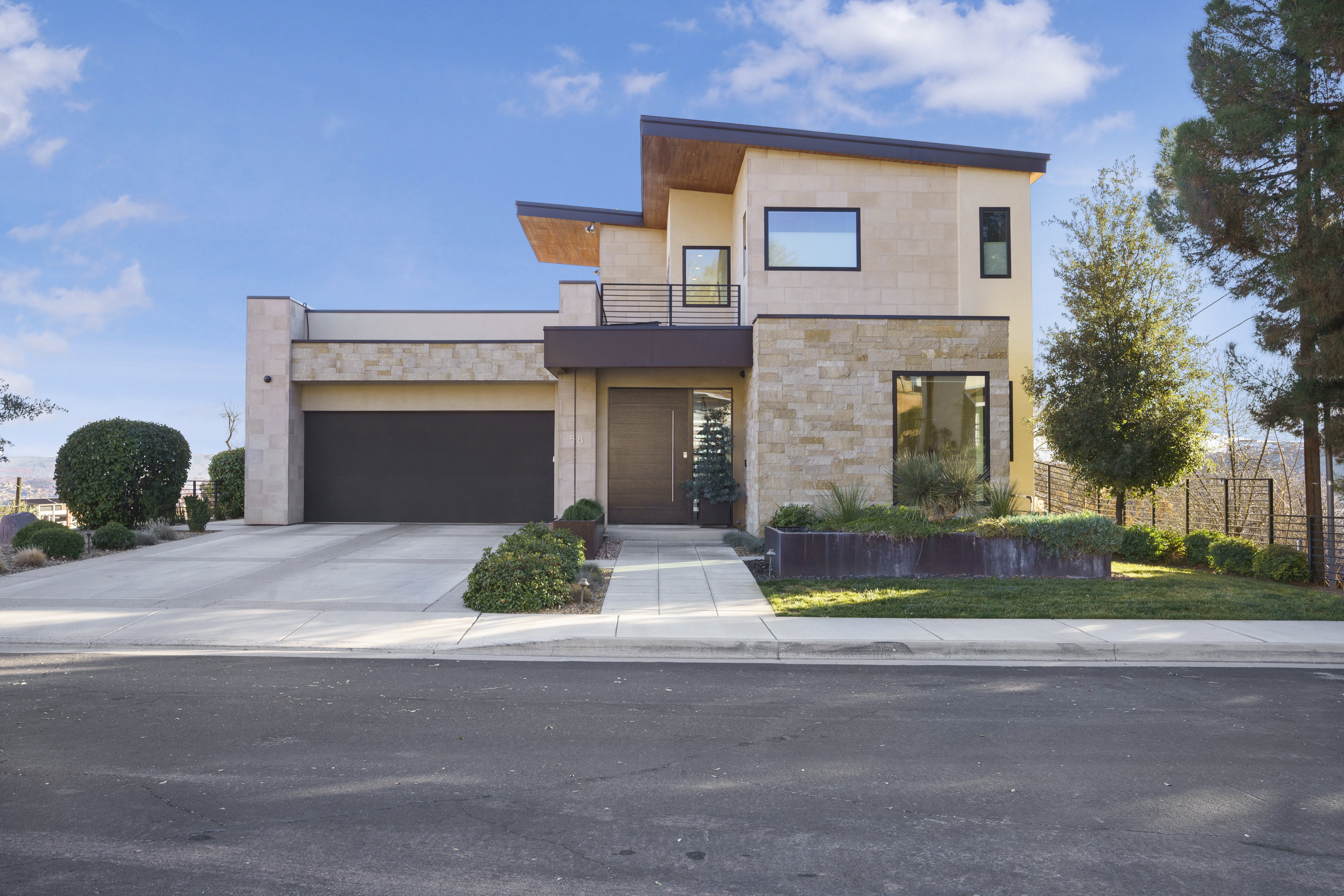 Contemporary house with stone siding, a balcony, and driveway