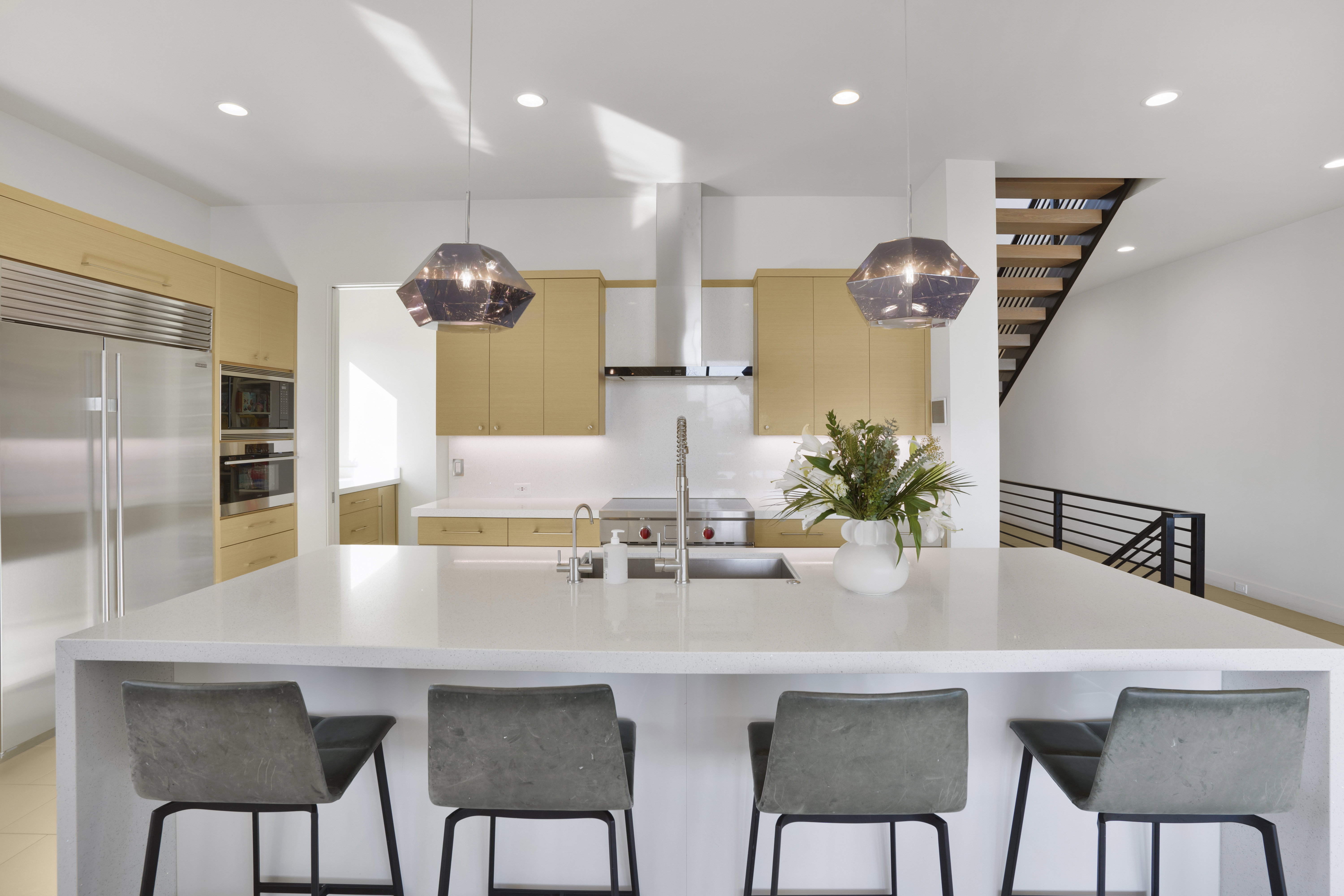 Kitchen with built in appliances, light stone counters, hanging light fixtures, a large island with sink, and a kitchen breakfast bar
