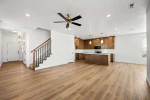 Kitchen with open floor plan, wood finish cabinets, pendant lighting, a kitchen island with sink, and a ceiling fan