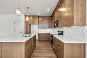 Kitchen featuring range with electric cooktop, wood finish cabinetry, an island with sink, pendant lighting, and decorative backsplash