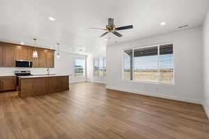 Kitchen with pendant lighting, open floor plan, stainless steel appliances, wood finish cabinets, and a center island with sink