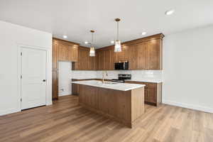 Kitchen featuring wood finish cabinets, decorative light fixtures, dark wood-type flooring, a kitchen island with sink, and stainless steel range with electric cooktop