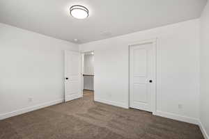 Unfurnished bedroom with dark carpet and baseboards