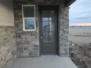 Exterior entry at dusk with stone siding and a patio area