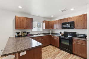 Kitchen featuring dark countertops, black appliances, a peninsula, light wood-style floors, and wood finish cabinetry