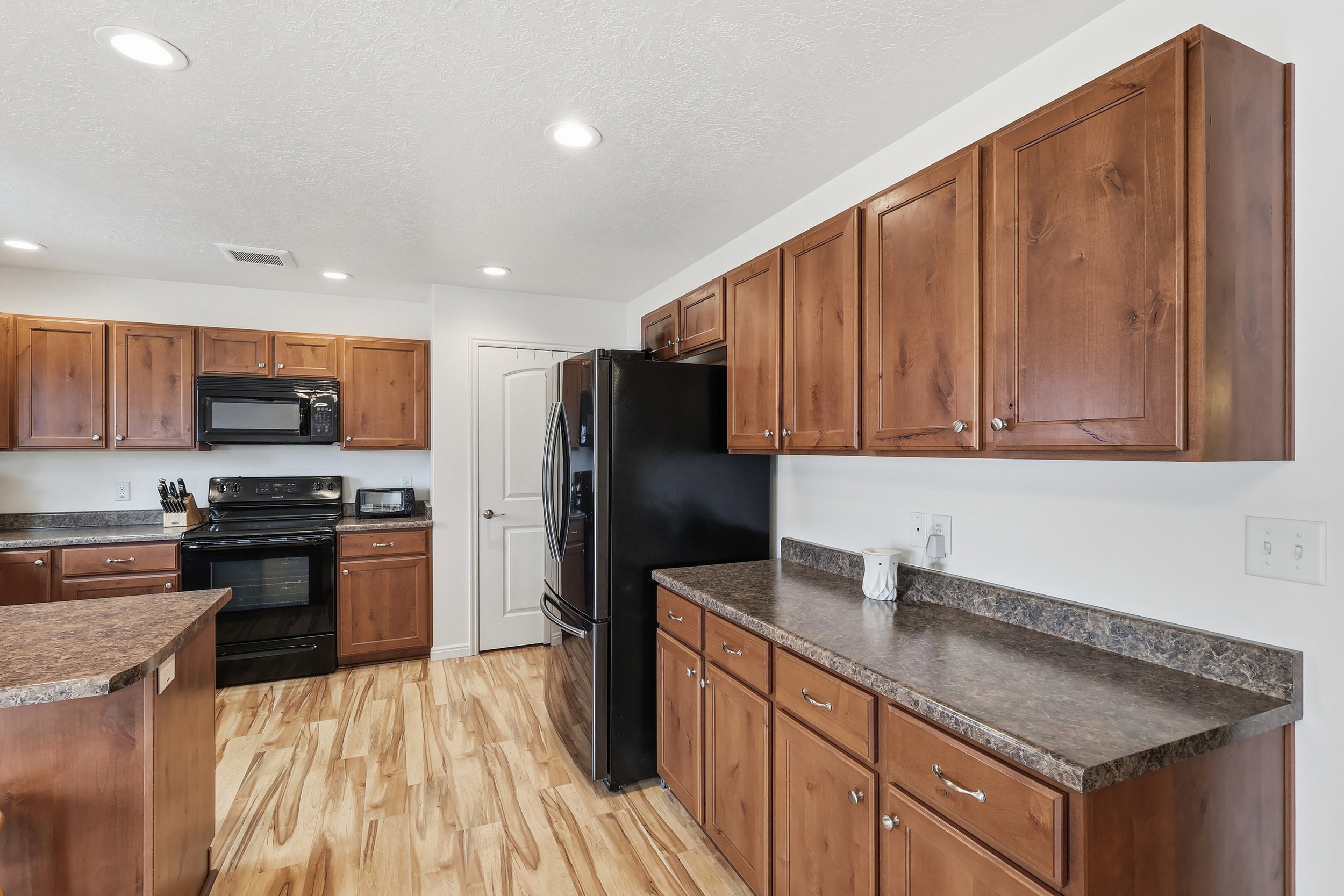Kitchen with dark countertops, black appliances, wood finish cabinets, light wood-style flooring, and recessed lighting