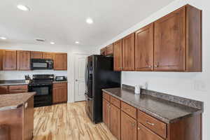 Kitchen with dark countertops, black appliances, wood finish cabinets, light wood-style flooring, and recessed lighting
