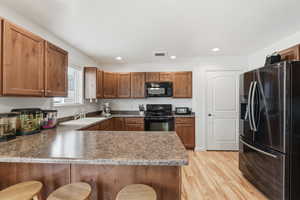 Kitchen with a breakfast bar area, black appliances, a peninsula, wood finish cabinets, and recessed lighting