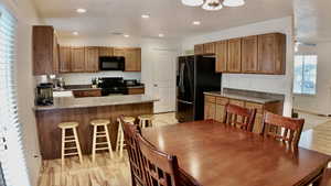 Kitchen featuring light wood-style floors, a peninsula, black appliances, a breakfast bar, and a textured ceiling