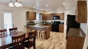 Kitchen featuring wood finish cabinets, black appliances, a peninsula, dark countertops, and a textured ceiling