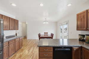 Kitchen featuring dark countertops, a peninsula, dishwasher, light wood-style flooring, and wood finish cabinets