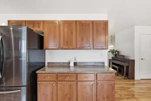 Kitchen with freestanding refrigerator, wood finish cabinets, dark countertops, and light wood-style flooring