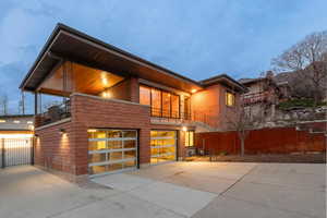 Modern home with driveway, an attached garage, gate, custom glass garage doors, and a balcony