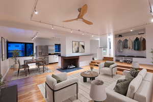 Living area with light wood-style flooring, ceiling fan, rail lighting, and a brick fireplace