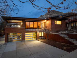 Back of property featuring concrete driveway, an attached garage with glass doors, a balcony, and brick siding