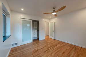 ensuite bedroom with ceiling fan, light wood-style floors, closet with opaque glass doors, and recessed lighting